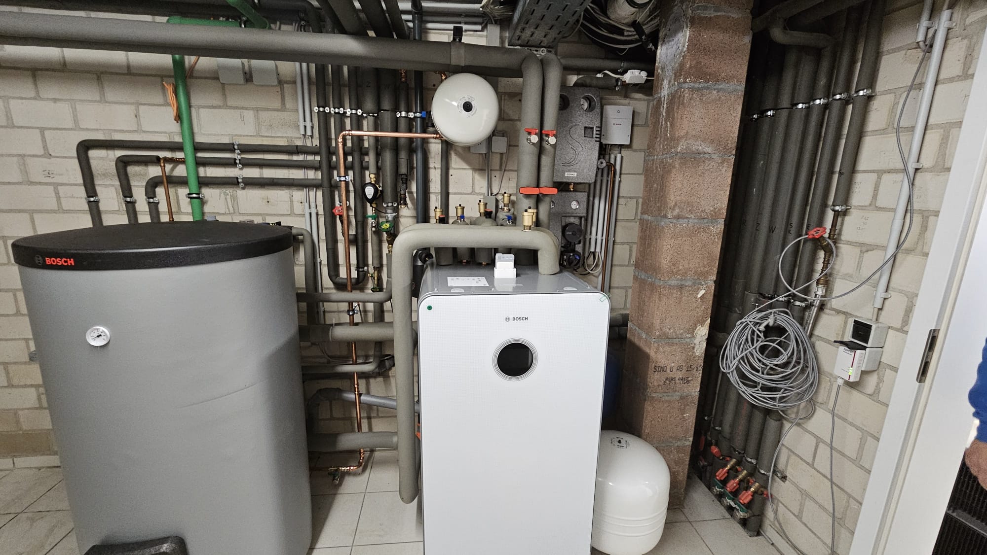 Bosch-Wärmepumpen-Inneneinheit mit umfangreicher Verrohrung und Speichertank in einem gut ausgestatteten Heizungsraum installiert.